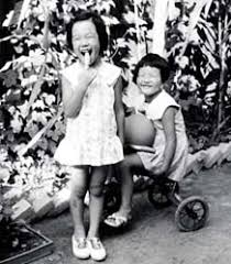 Tomoko Watanabe (left), as a child in elementary school, stands in front of corn she helped grow in the family garden. - img_01